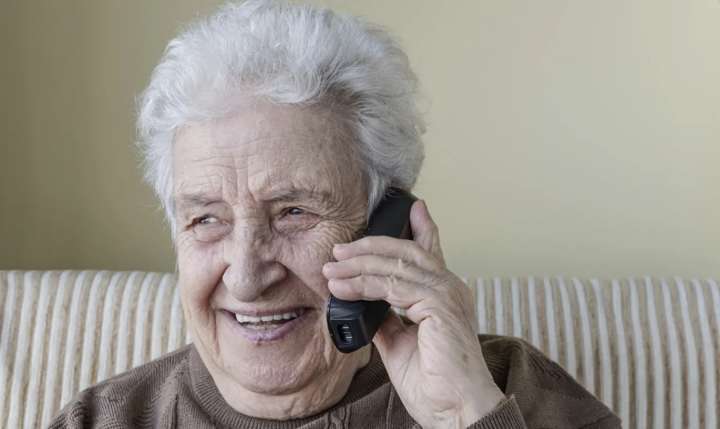 A smiling older woman with white hair chatting happily on the phone at home